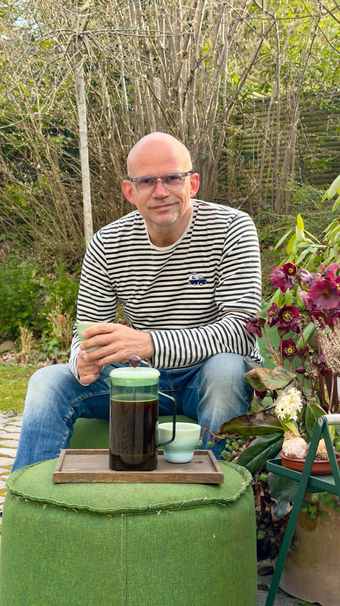 Jesper Vollmer i haven med en kop kaffe og HAYs stempelkande i aqua på en træbakke foran sig