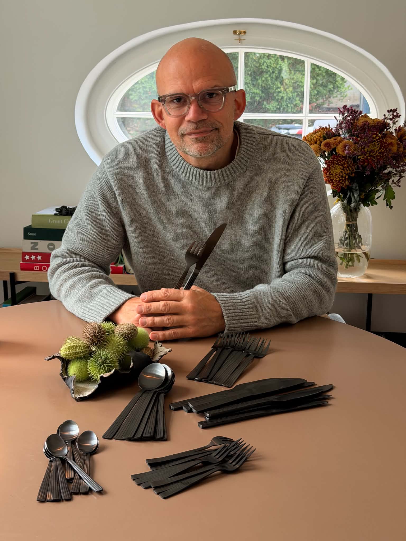 Jesper Vollmer ved et rundt bord med en kniv og en gaffel i hånden og det mat sorte RAW-bestik lagt frem i bunker foran sig