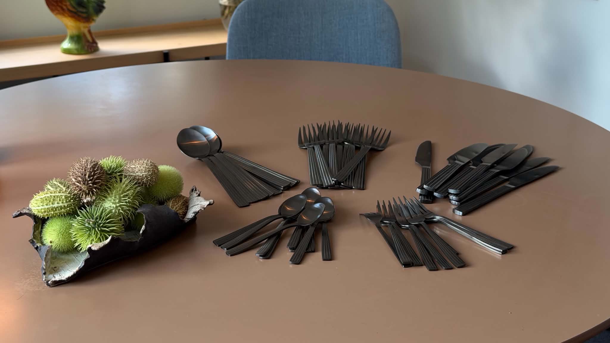 Det mat sorte RAW-bestik sorteret i bunker med knive, gafler, spiseskeer, kaffeskeer og kagegafler på et rundt bord
