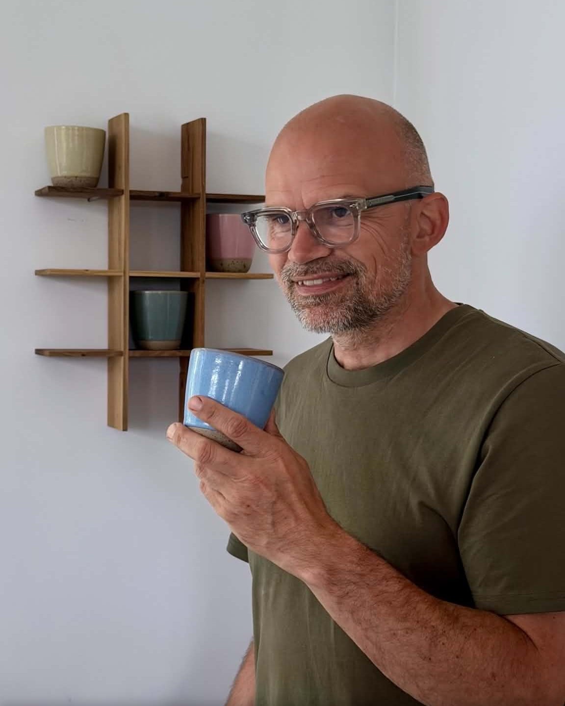 Jesper Vollmer med et blåt Raw Colour krus foran Raw Teak reolen på væggen